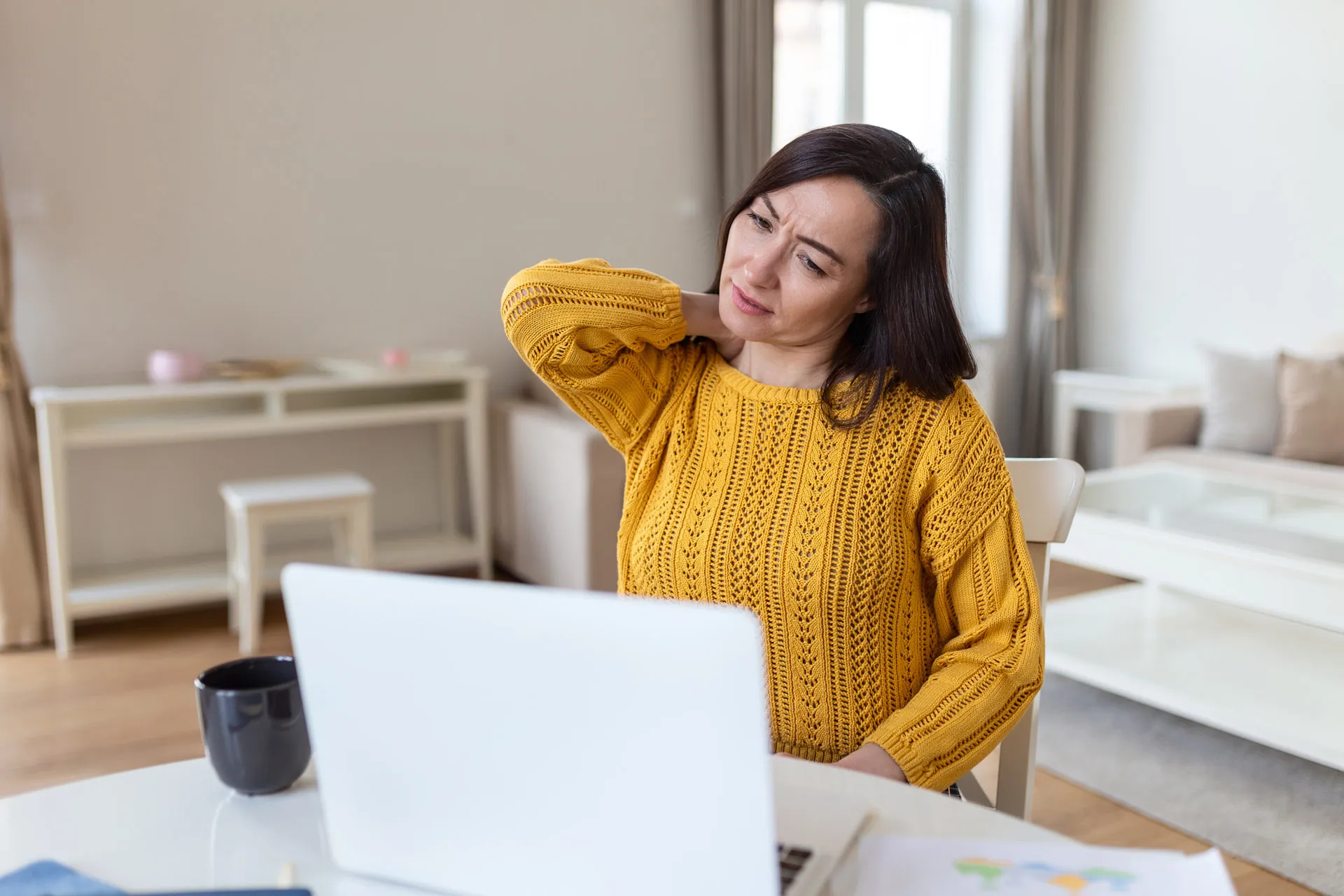 Eine Frau arbeitet zuhause am Laptop und fasst an den Nacken.